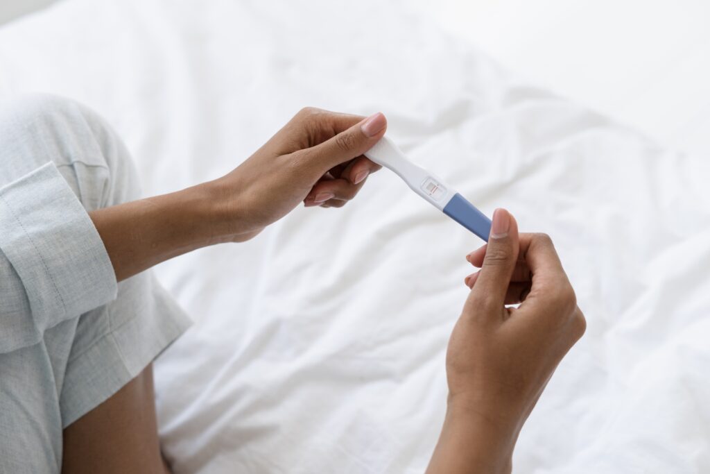 close up of a woman's hands holding a pregnancy test over a white sheet