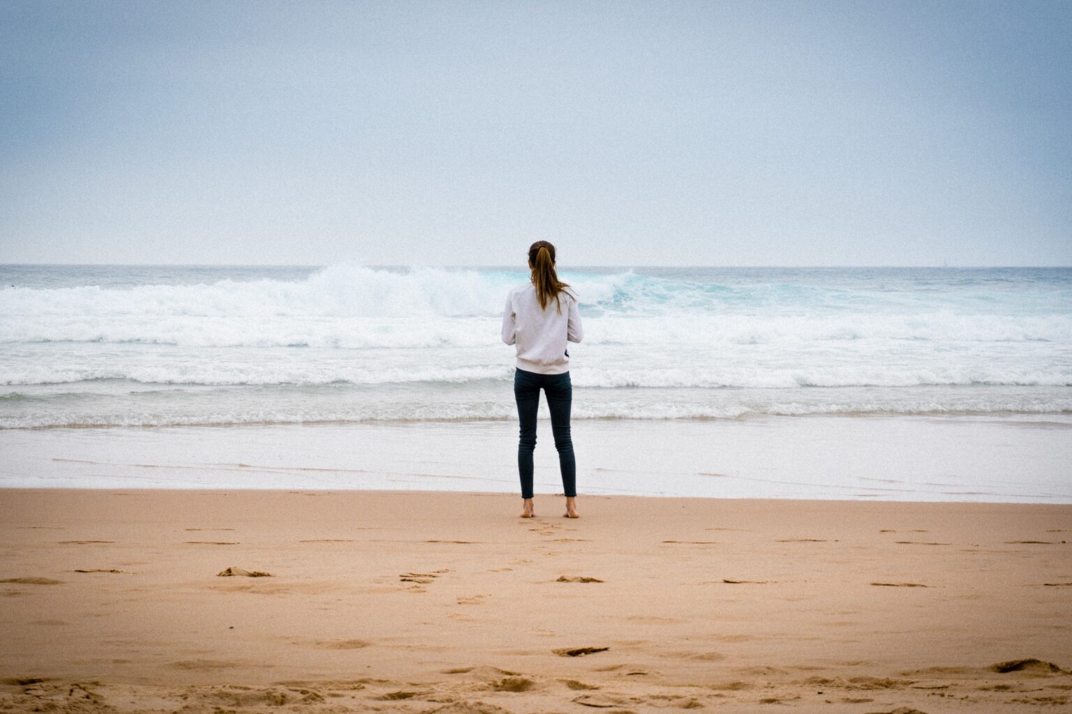 a young woman standing on a beach looking at the ocean