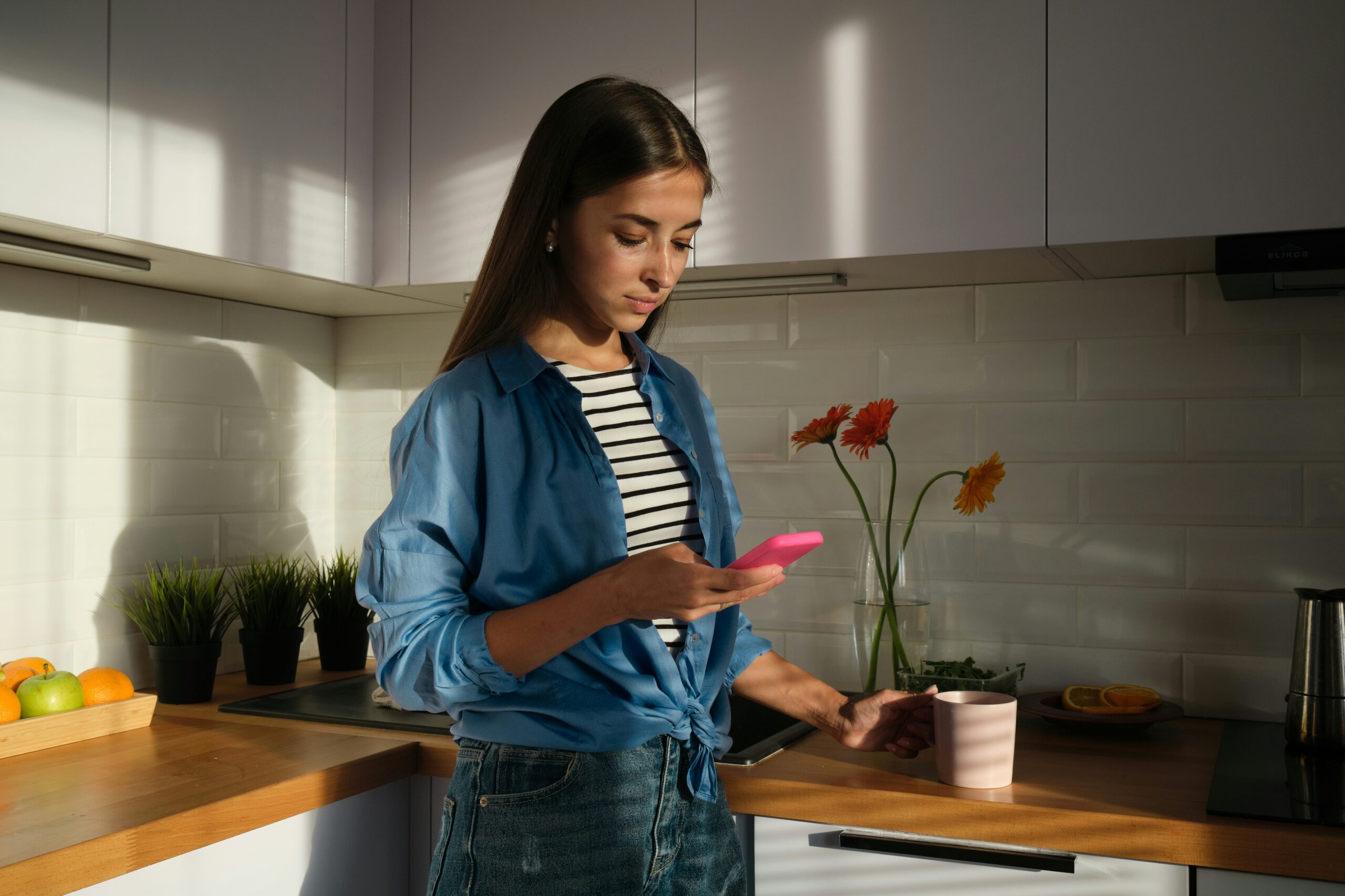 a young woman standing in her kitchen searching on her phone