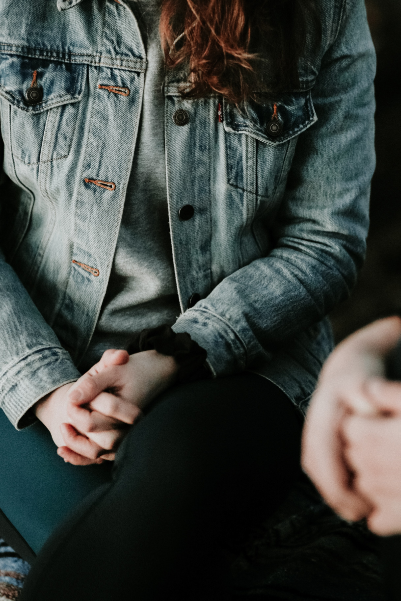 person in jean jacket with hands clasped in lap