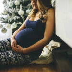 Pregnant woman sitting in front of a Christmas tree.